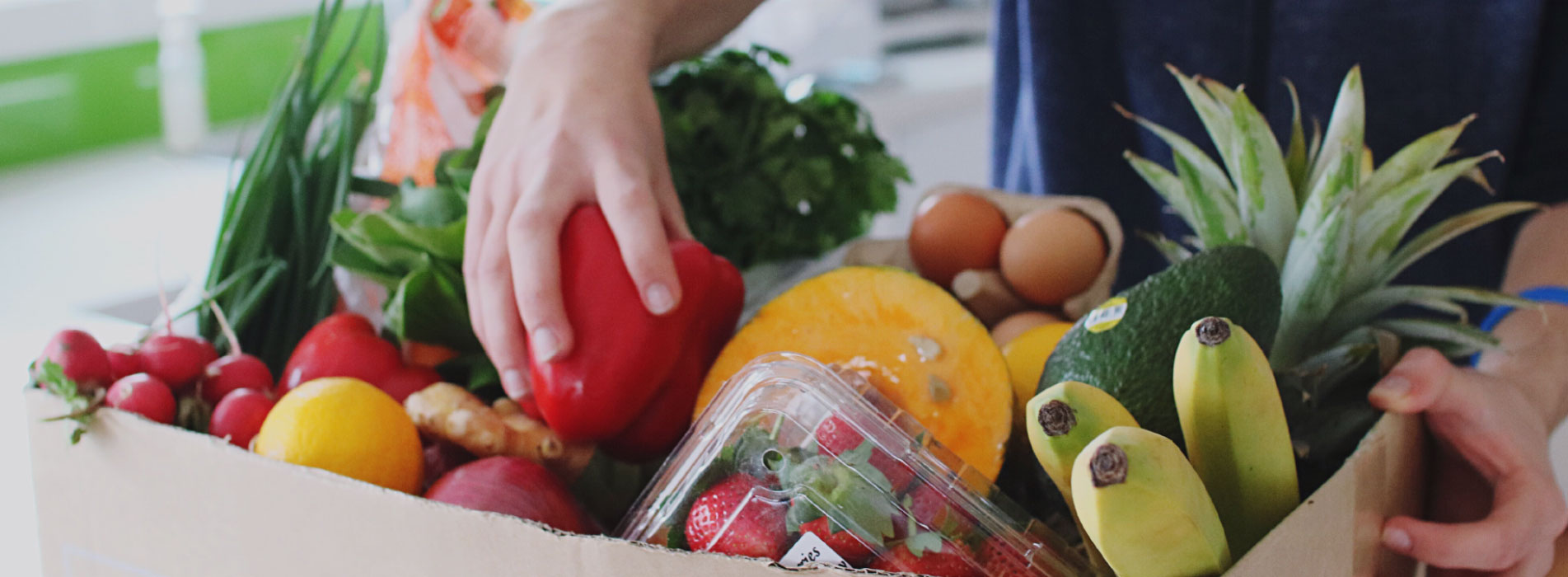 Packing up a delivery of fresh fruit and veg bananas, pineapple, avocado, strawberries, pepper, tomatoes, oranges, melon, eggs, carrots